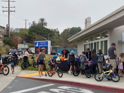 A large group of kids and parents on bikes in front of Paul Ecke Elementary School